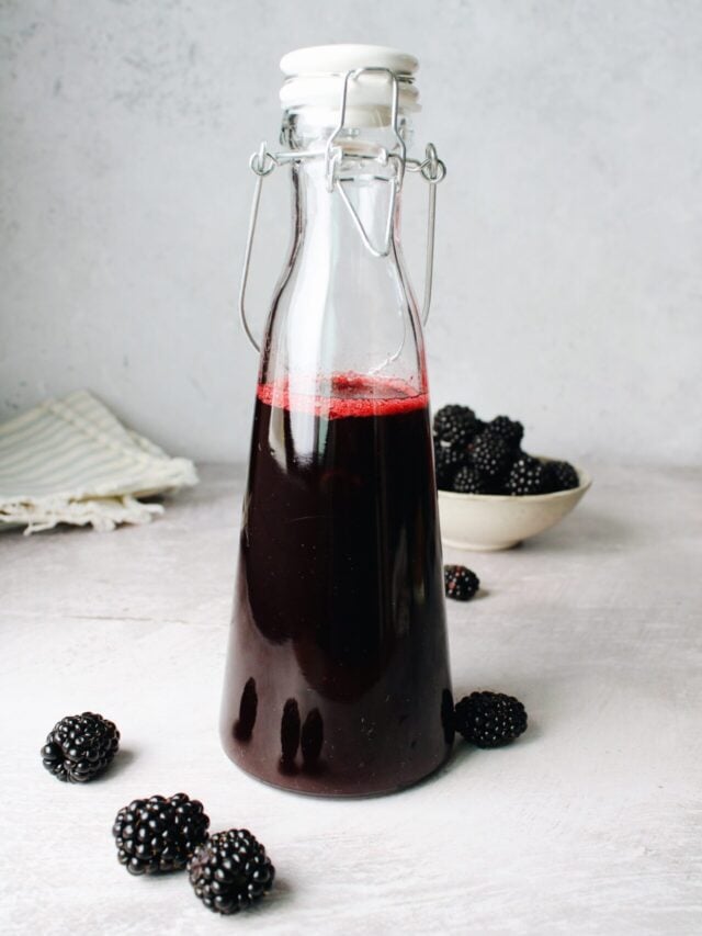 blackberry simple syrup in a glass bottle with blackberries scattered around