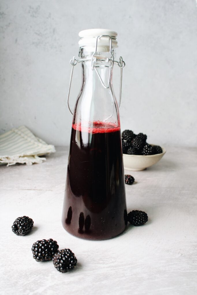 blackberry simple syrup in a glass bottle with blackberries scattered around