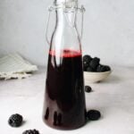blackberry simple syrup in a glass bottle with blackberries scattered around