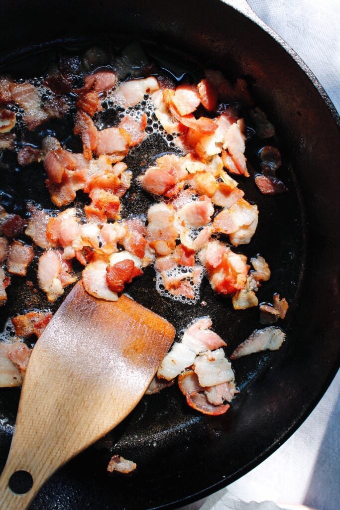 bacon pieces cooking in a cast iron pan