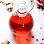 rose simple syrup in a glass jar with rose petals scattered around