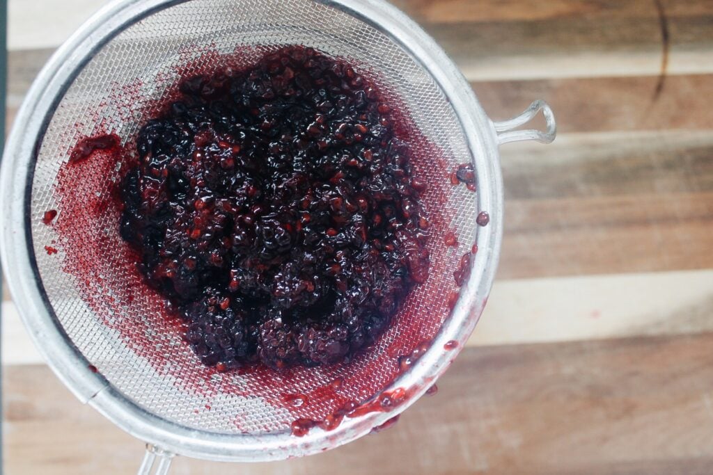 blackberry simple syrup mixture being put through a fine mesh sieve