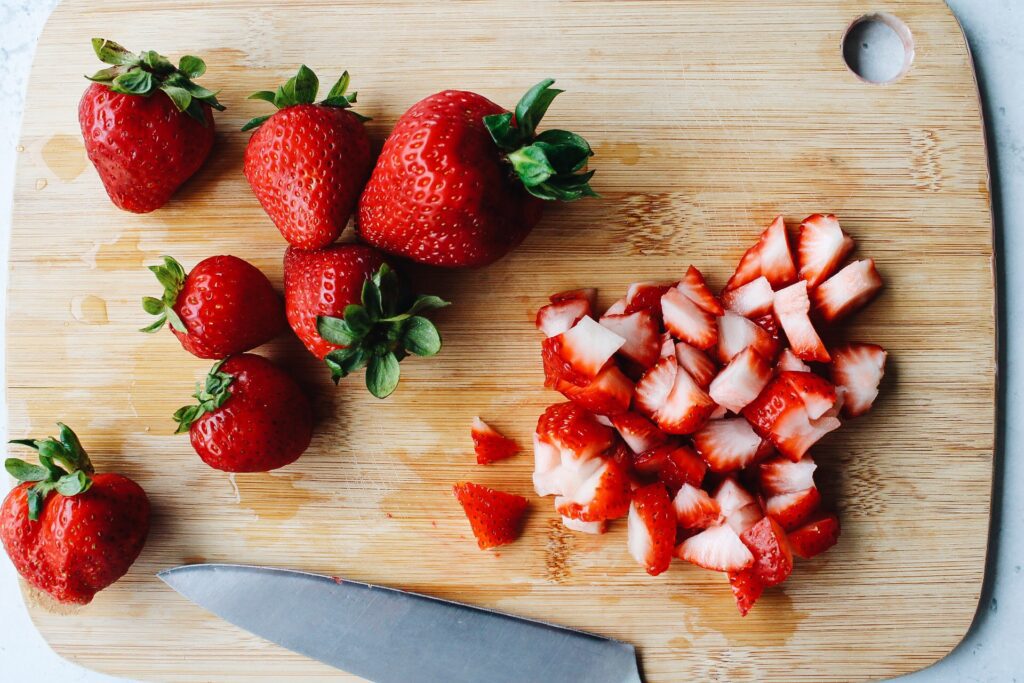whole strawberries and chopped strawberries on a wooden cutting board
