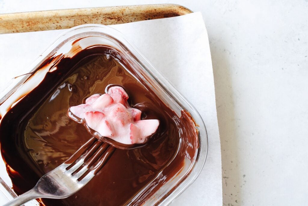 frozen berry yogurt cluster being dipped in chocolate