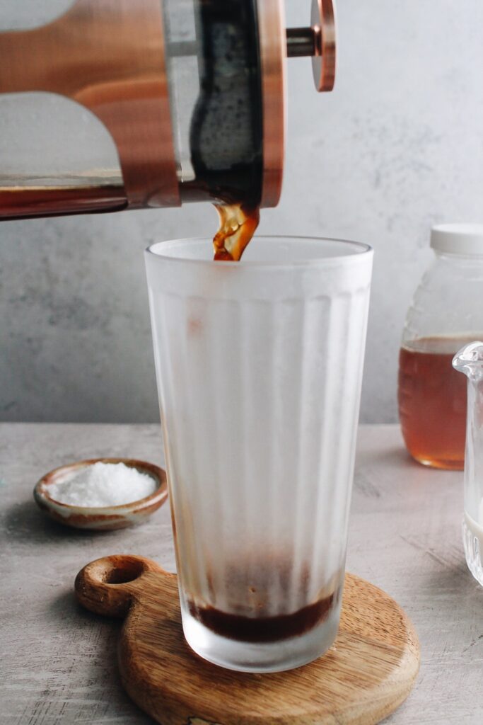 coffee being poured from a french press into a tall clear glass