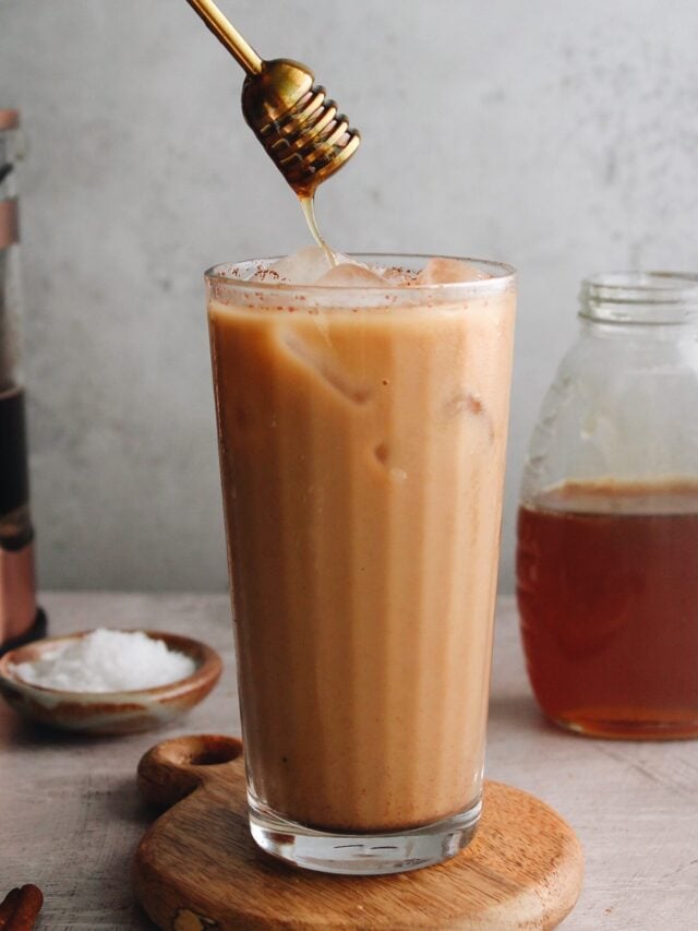 an iced honey cinnamon latte in a clear glass with a honey dipper drizzling honey