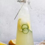cucumber lemonade in clear glass bottle with lemon wedges scattered around