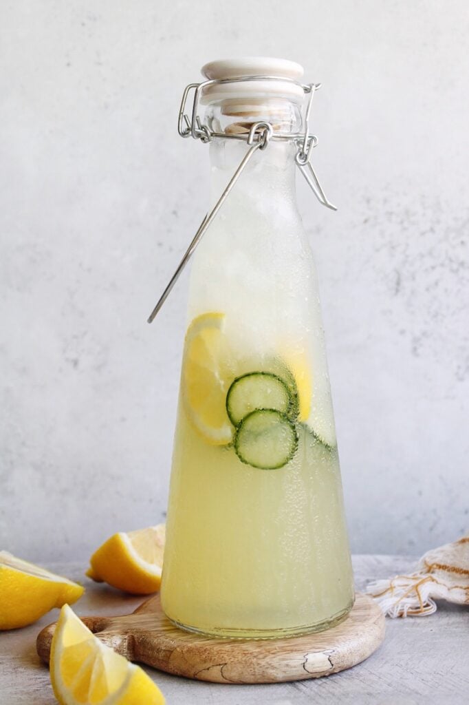 cucumber lemonade in clear glass bottle with lemon wedges scattered around