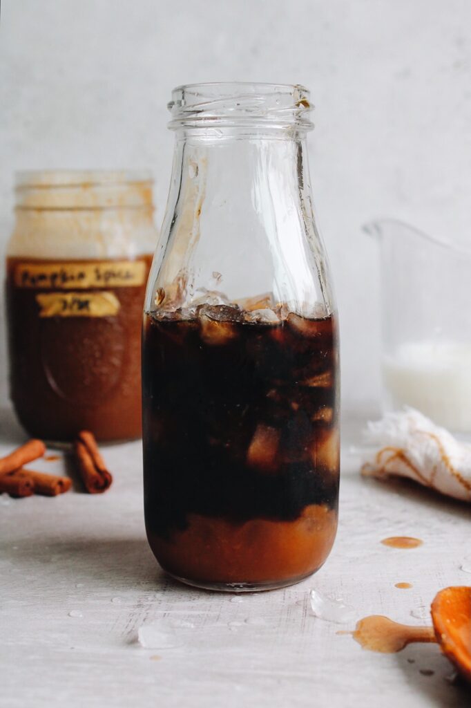 partially made pumpkin spice iced coffee in a glass bottle