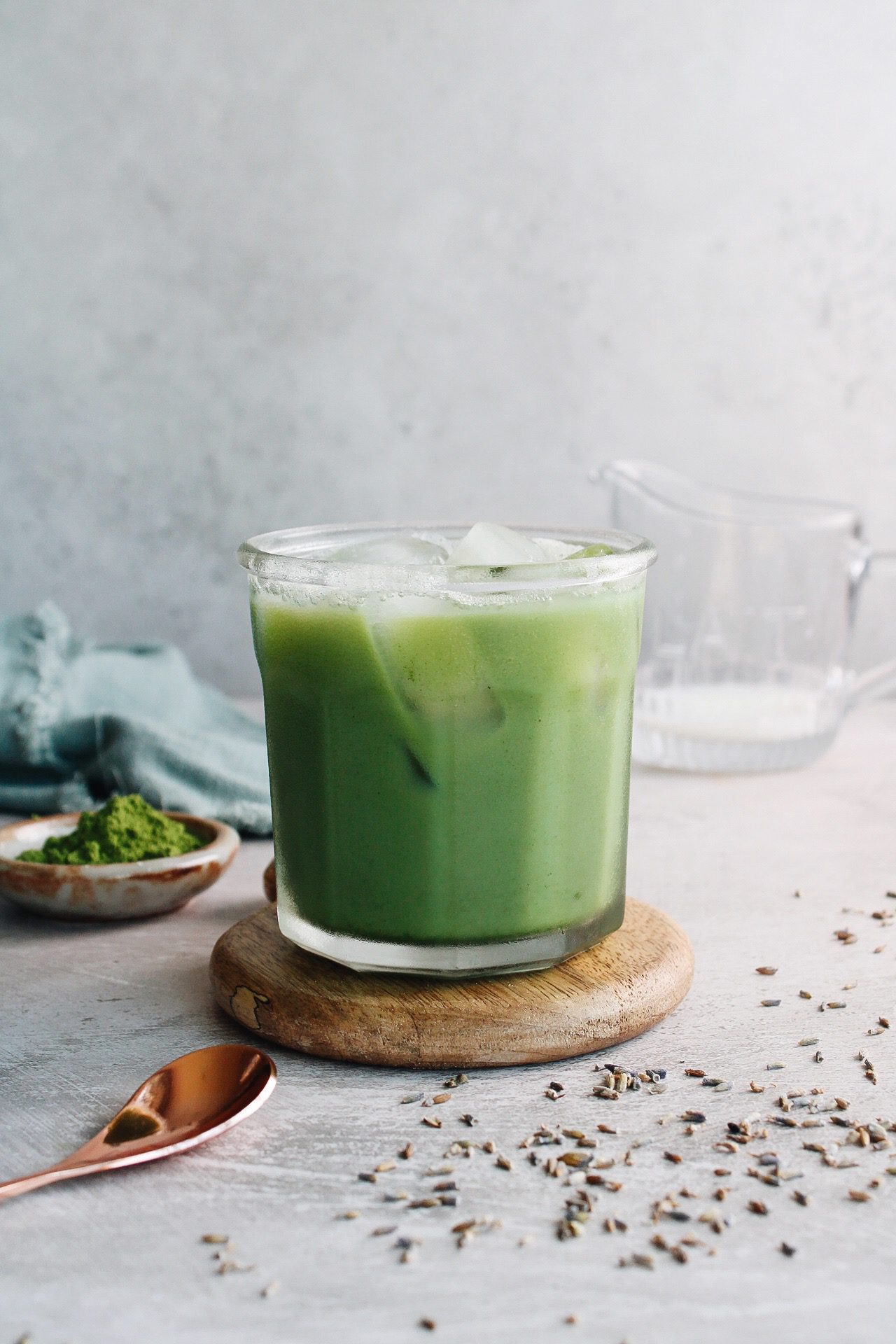 lavender matcha latte in a clear glass with lavender flowers scattered around