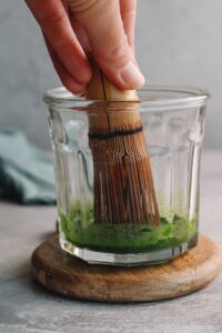matcha in a wide-mouthed glass being whisked