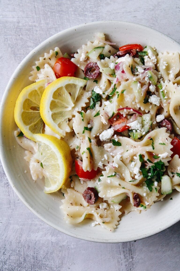 close up of mediterranean pasta salad in a white bowl topped with lemons