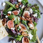 fig salad with goat cheese and candied walnuts on a gray plate with a slice of bread