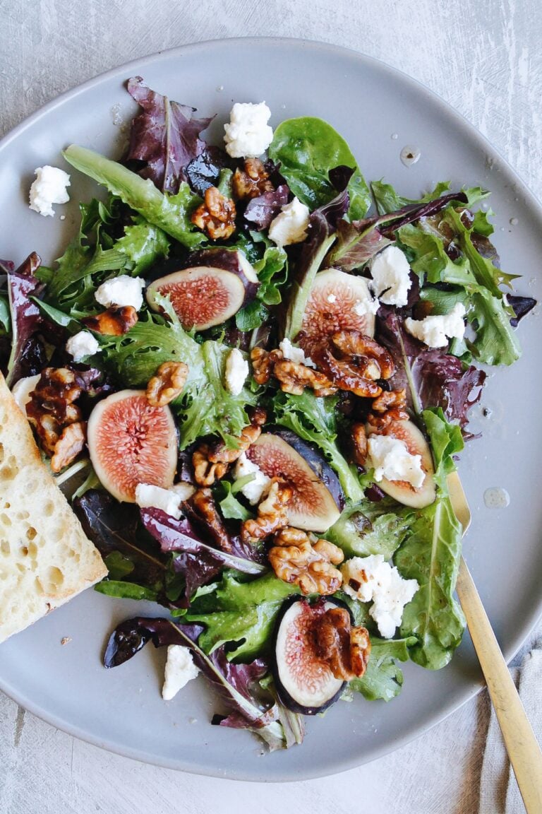 fig salad with goat cheese and candied walnuts on a gray plate with a slice of bread