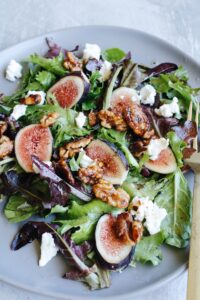fig salad with goat cheese, candied walnuts and vinaigrette on a gray plate