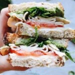 close up of pesto turkey sandwich with provolone, tomatoes and mixed greens