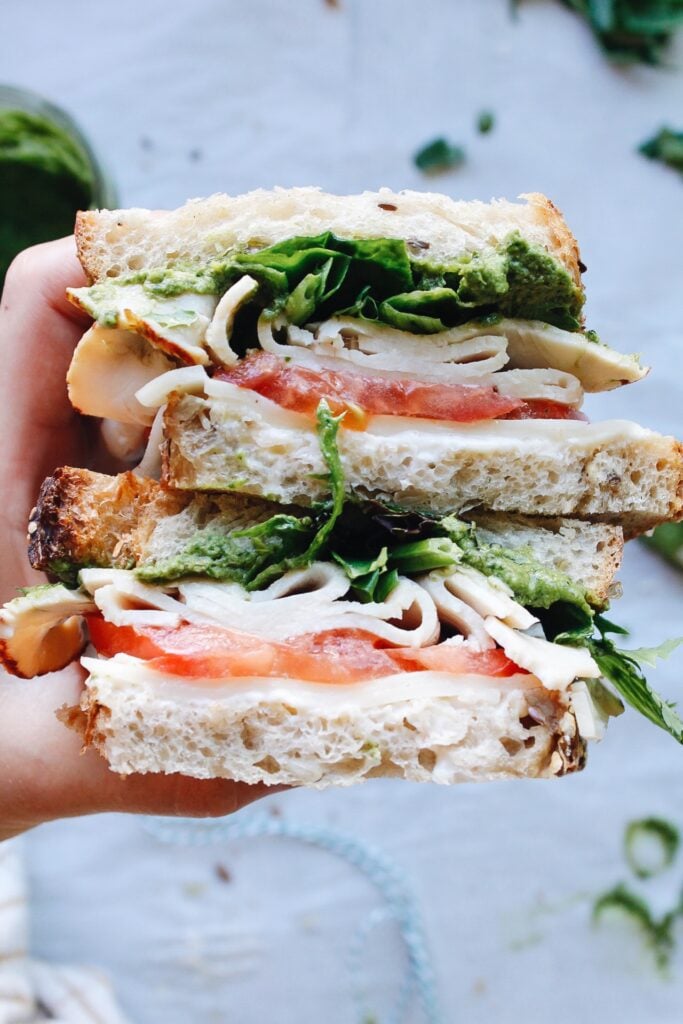 close up of pesto turkey sandwich with provolone, tomatoes and mixed greens