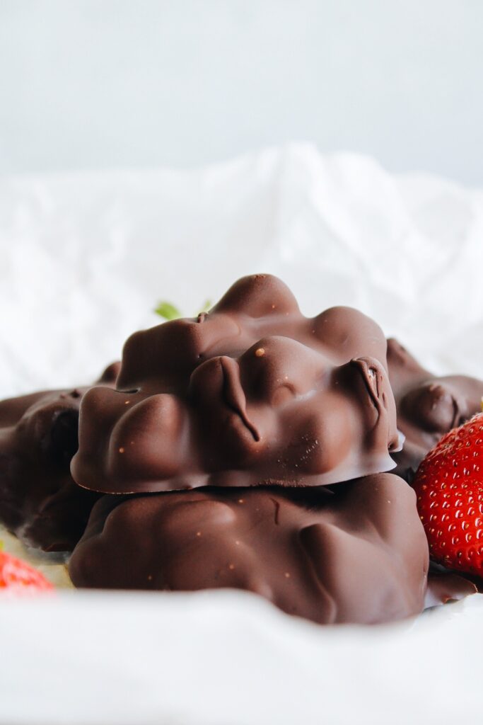 chocolate covered yogurt bites stacked on parchment paper with strawberries scattered around.