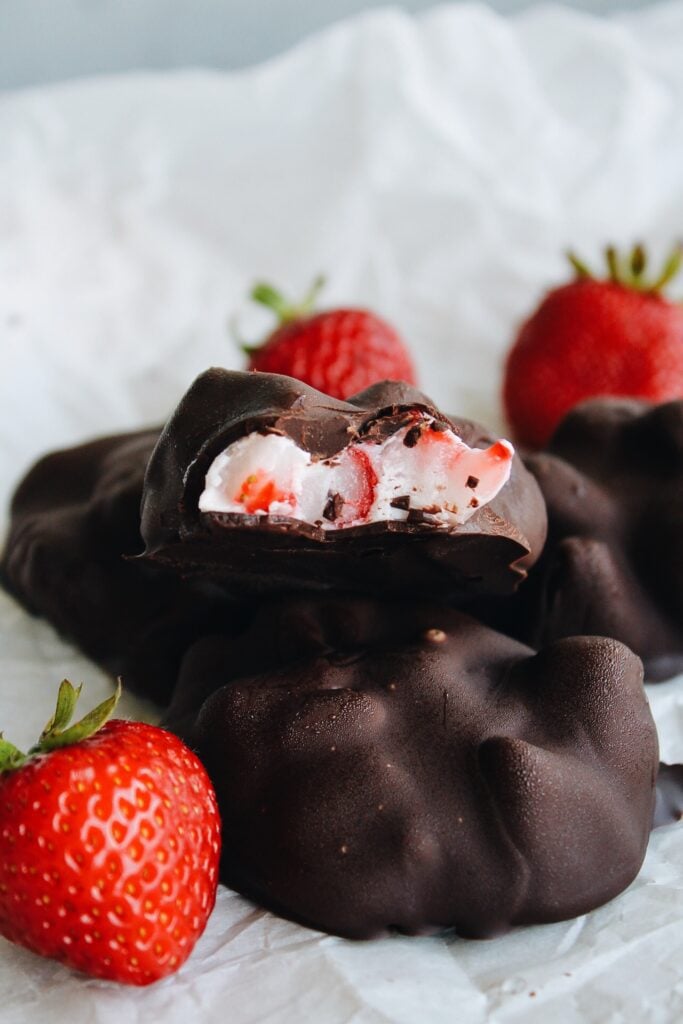 chocolate covered yogurt bites with a bite taken out of it to expose the yogurt and fruit inside