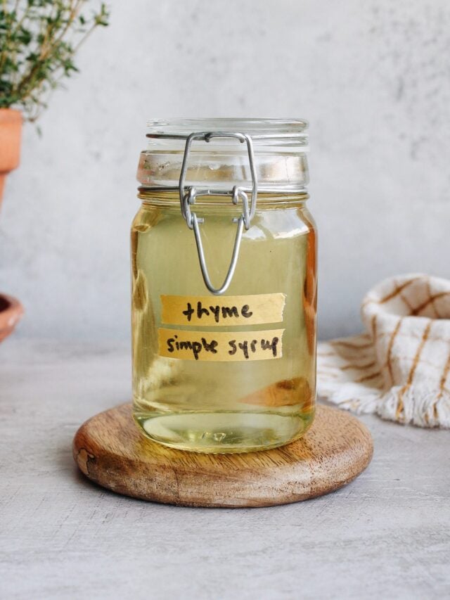 thyme simple syrup in a clear glass jar sitting on a white coaster