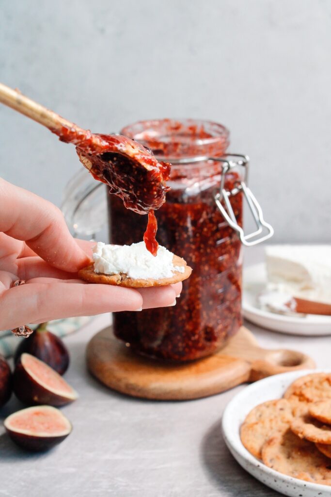 fig jam being added to a cracker with goat cheese