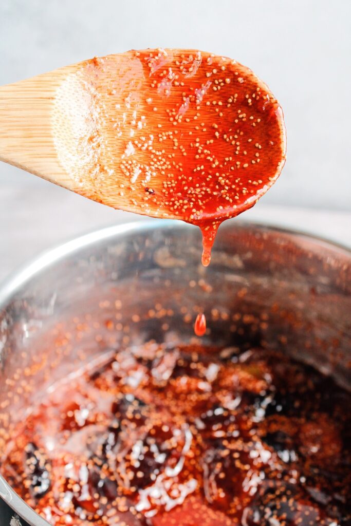 a wooden spoon with jam dripping into a pot