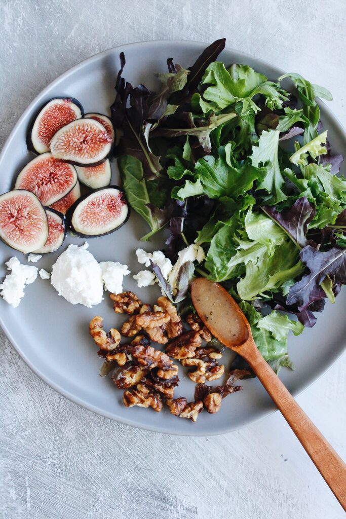 fig salad ingredients on a plate: fresh figs, goat cheese, mixed greens and candided walnuts