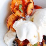 grilled peaches in a bowl topped with vanilla ice cream and mint