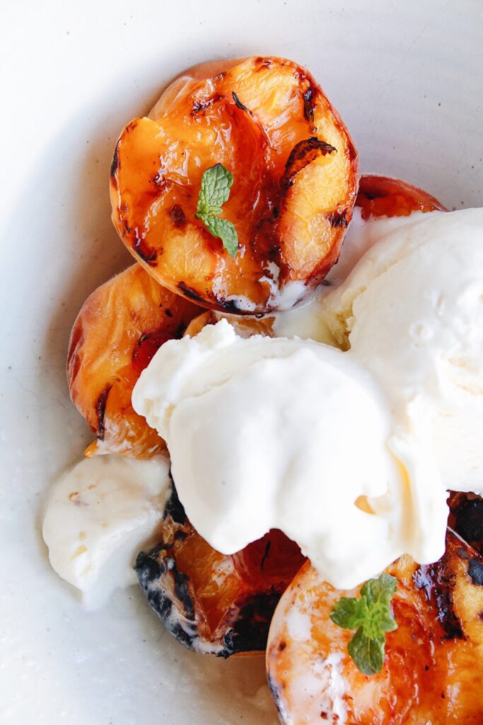 grilled peaches in a bowl topped with vanilla ice cream and mint