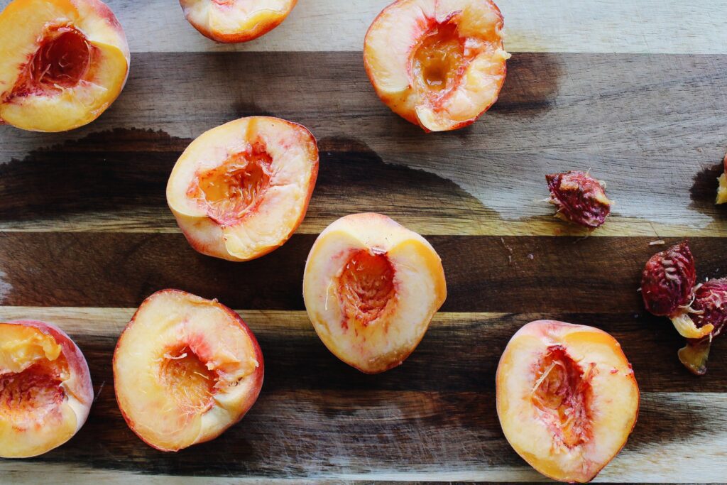 halved + pitted peaches on a wooden cutting board