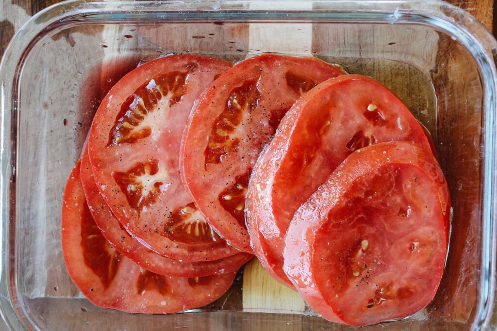 sliced tomatoes in a bowl with vinegar, oil, salt and pepper