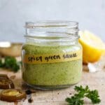 spicy green sauce in a glass jar on a wooden cutting board