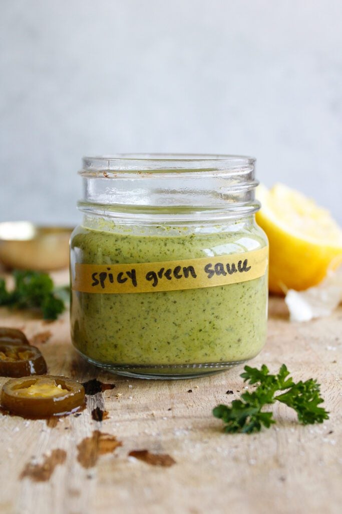 spicy green sauce in a glass jar on a wooden cutting board