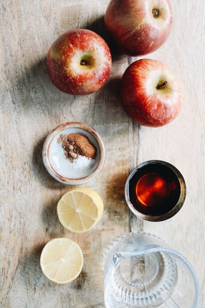 ingredients for apple cinnamon compote on a cutting board: apples, cinamon, lemon, water and maple syrup