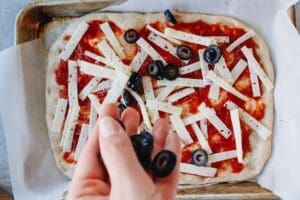 pizza dough being topped with sauce, cheese and olives