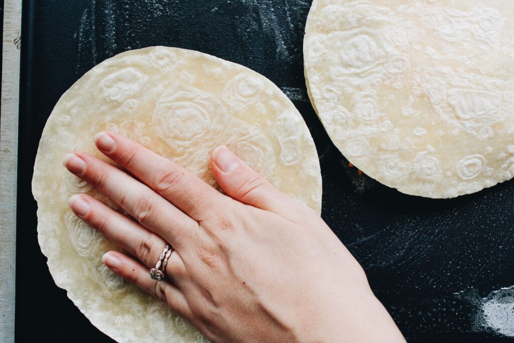 a hand pressing down on quesadilla cooking on a griddle