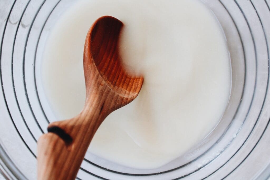 yeast dissolved in warm water being stirred with a wooden spoon