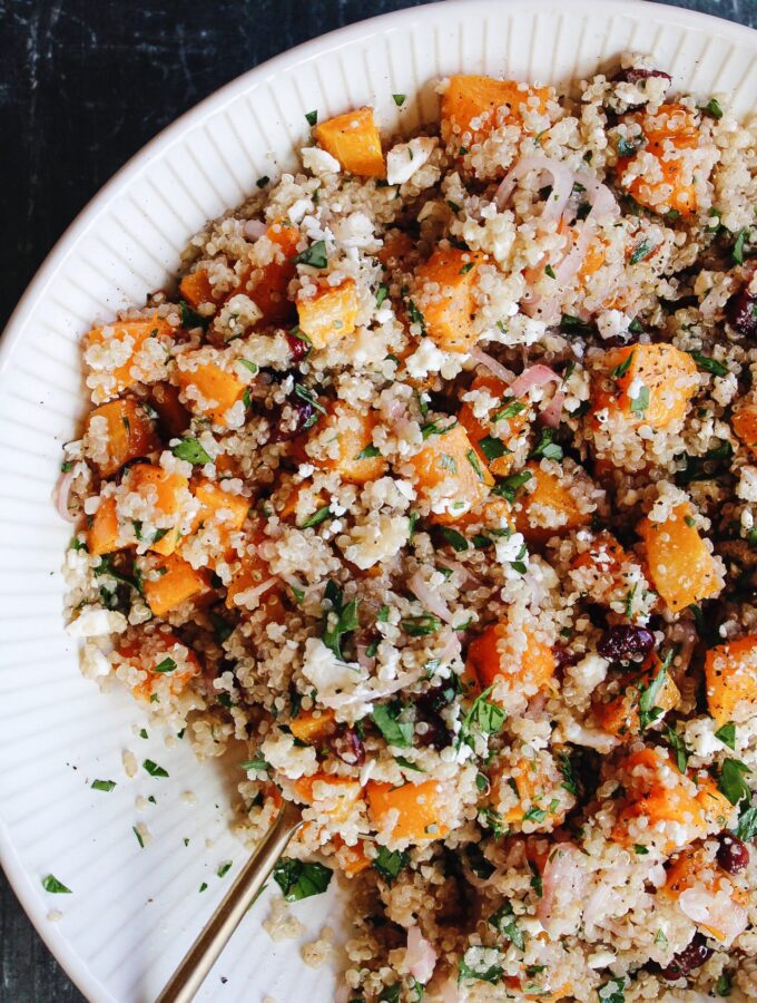 butternut squash quinoa salad in a beige bowl with gold serving spoon