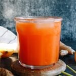 carrot ginger turmeric juice in a clear glass on a wooden coaster