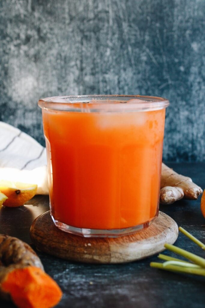 carrot turmeric juice in a clear glass on a wooden coaster