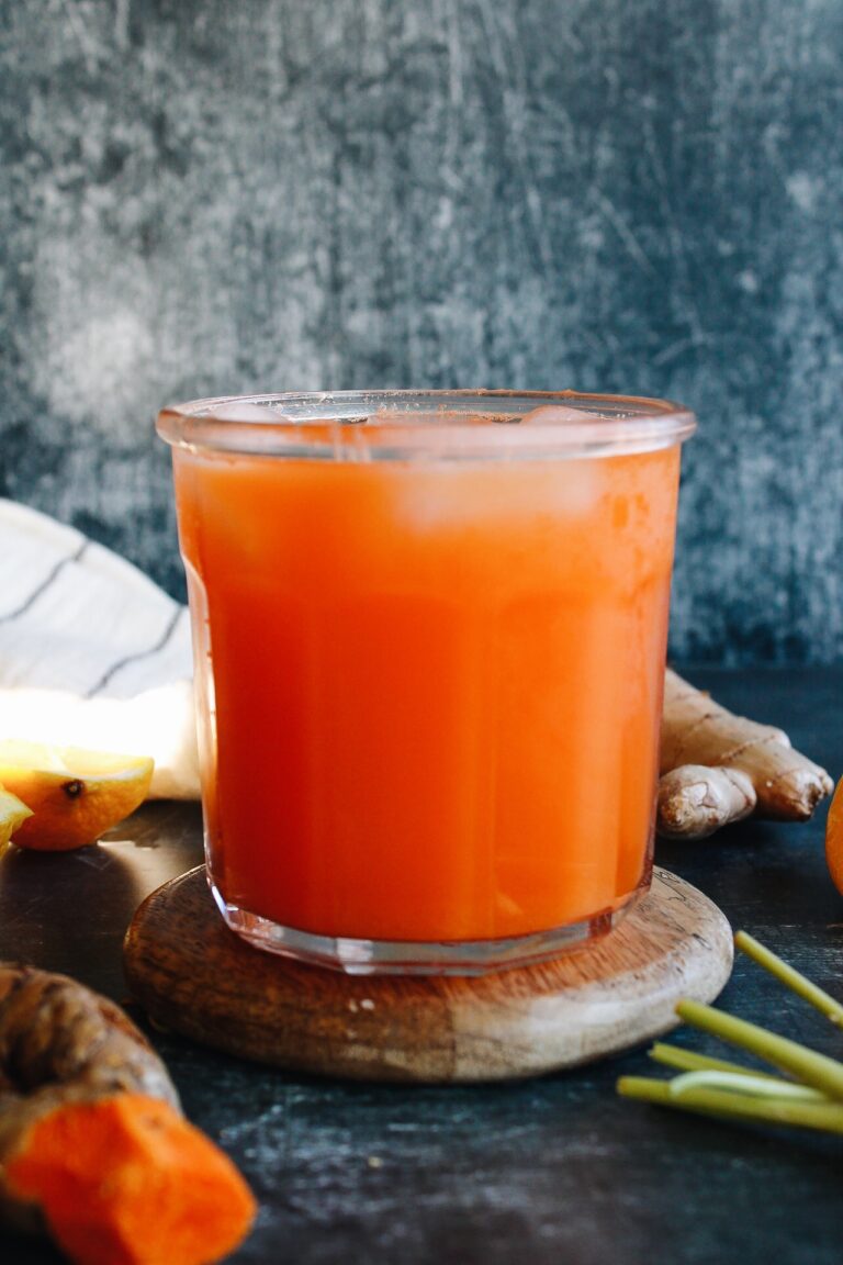 carrot ginger turmeric juice in a clear glass on a wooden coaster