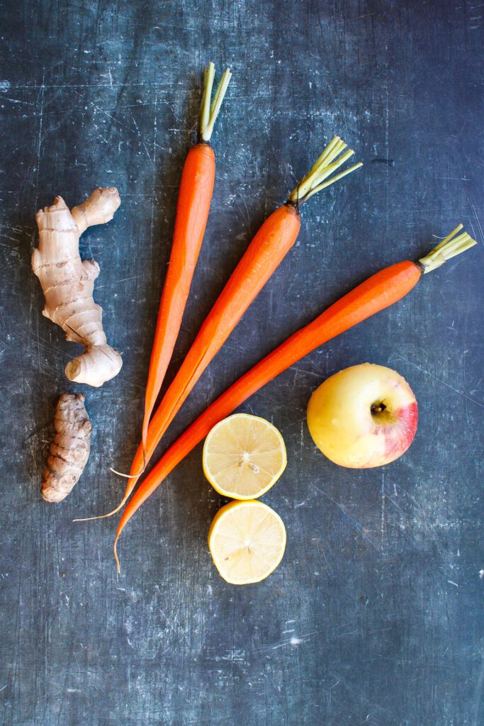 carrots, ginger, turmeric root, lemon and apple on a blue background