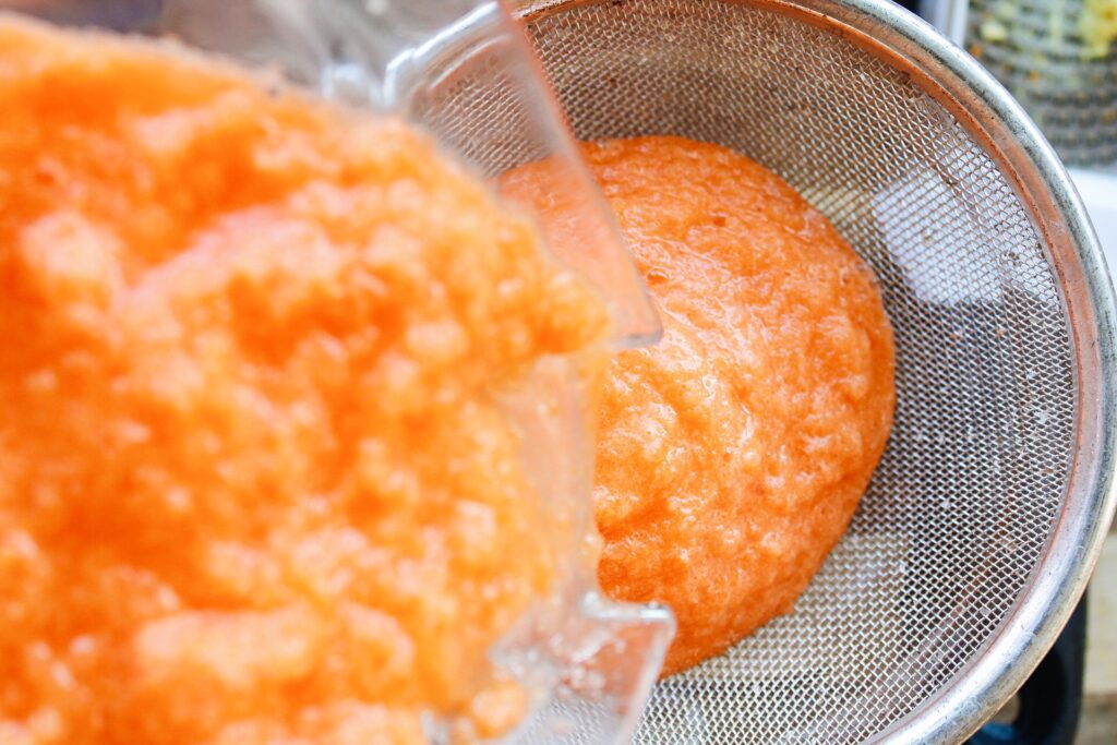 carrot turmeric juice pulp being poured through a strainer