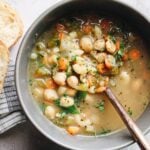 chickpea noodle soup in a gray bowl next to bread
