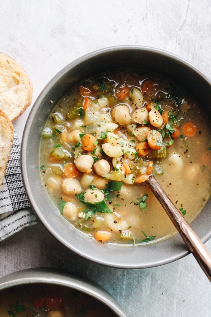 chickpea noodle soup in a gray bowl next to bread