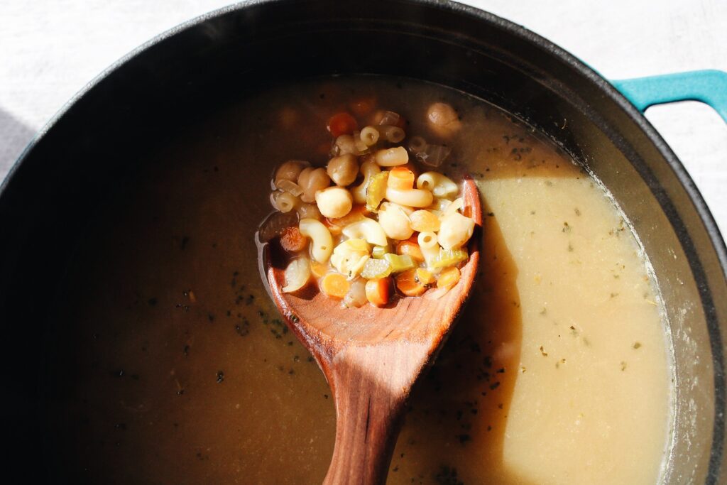 chickpea noodle soup on a wooden spoon over a pot
