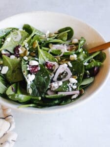 spinach and goat cheese salad with cranberries and pepitas in a white bowl
