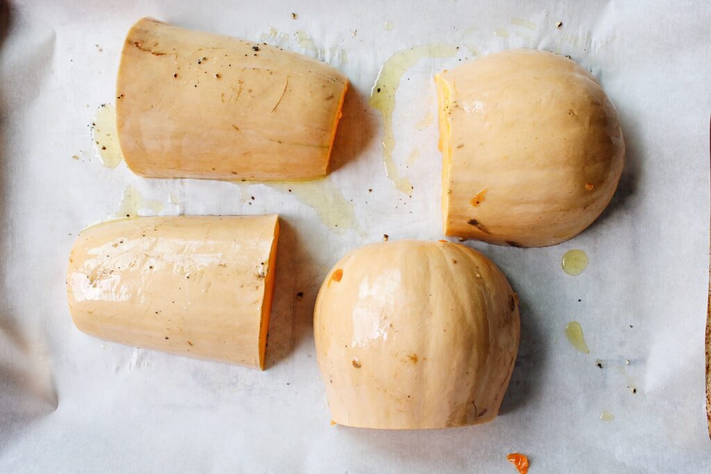 butternut squash cut into quarters face down on a baking sheet lined with parchment
