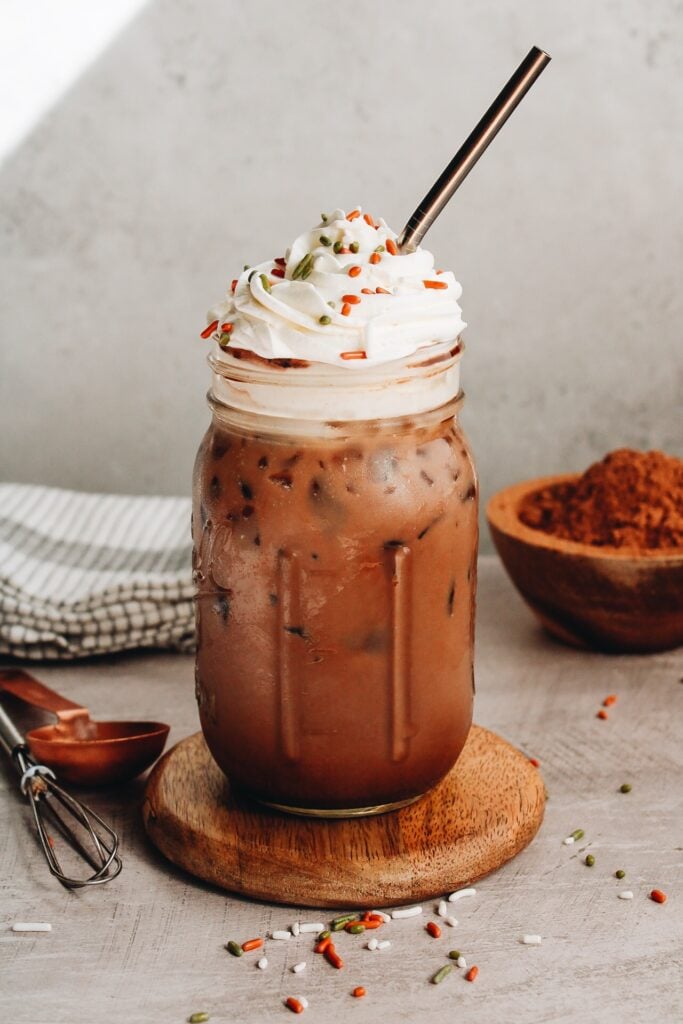 an iced peppermint mocha in a mason jar topped with sprinkles and whipped cream