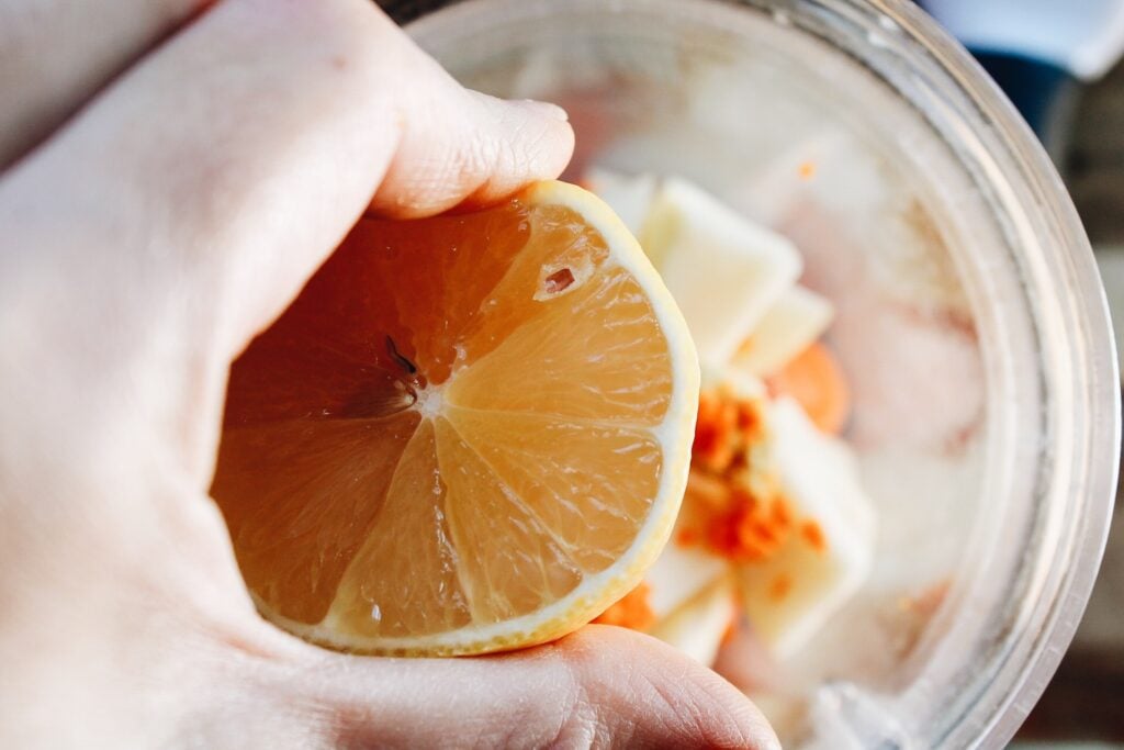 a cut lemon being squeezed over a blender